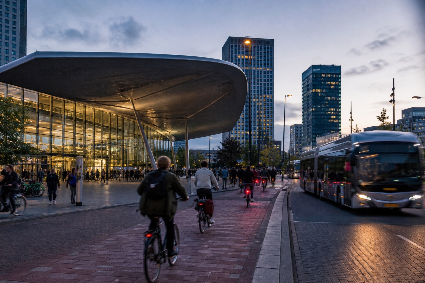Stationsplein bij schemer met fietsers, voetgangers en een bus