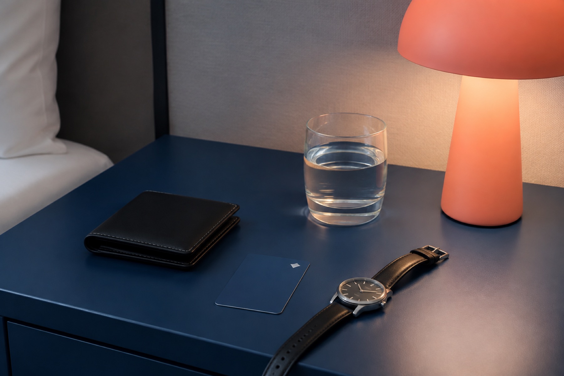 Nachtkastje met portemonnee, horloge en een glas water naast een lamp